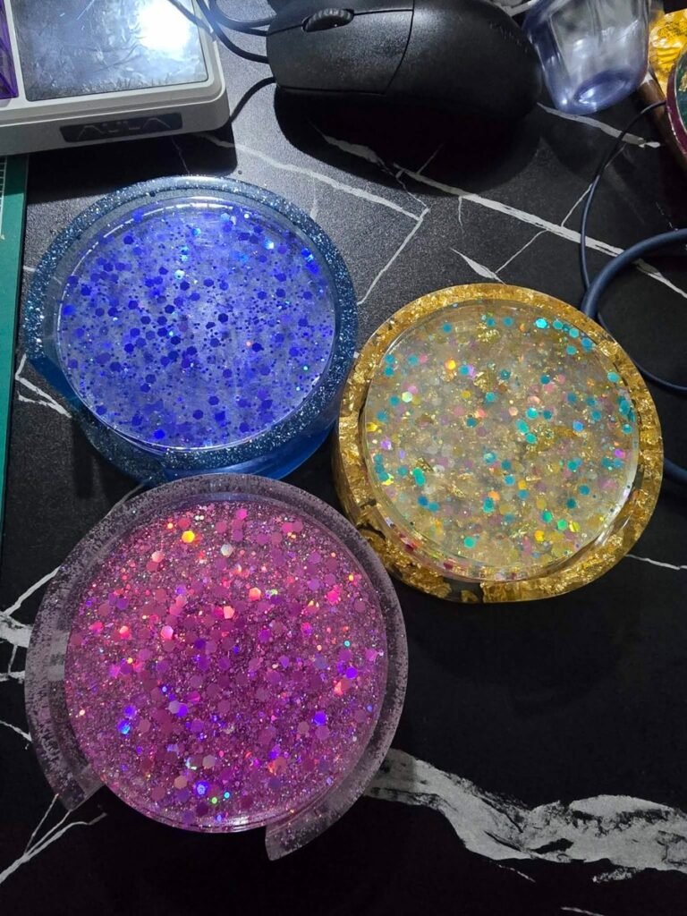 Three resin coasters showing blue glitter, holographic gold confetti, and pink glitter colorways
